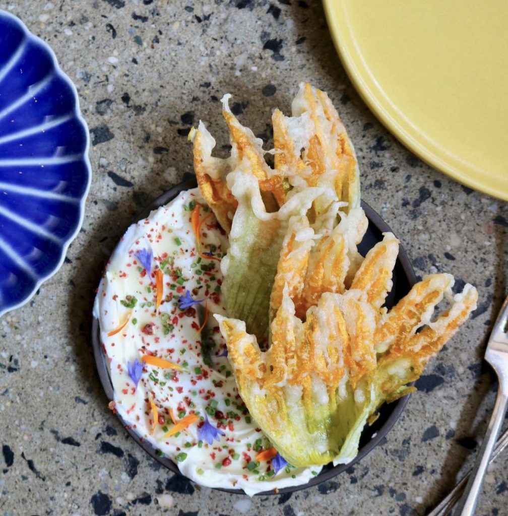 Crispy green leaves on colorful blue plate on stone table at Shukette.